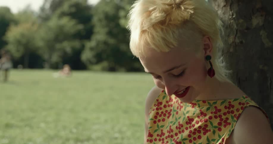Young short haired blonde woman sitting under a tree over the grass at a park