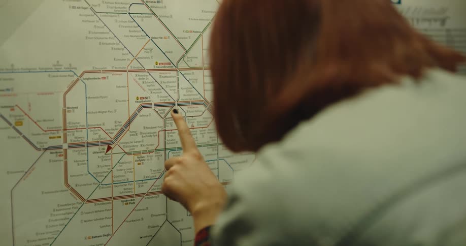 A woman runs her finger along a map of train lines in a terminal