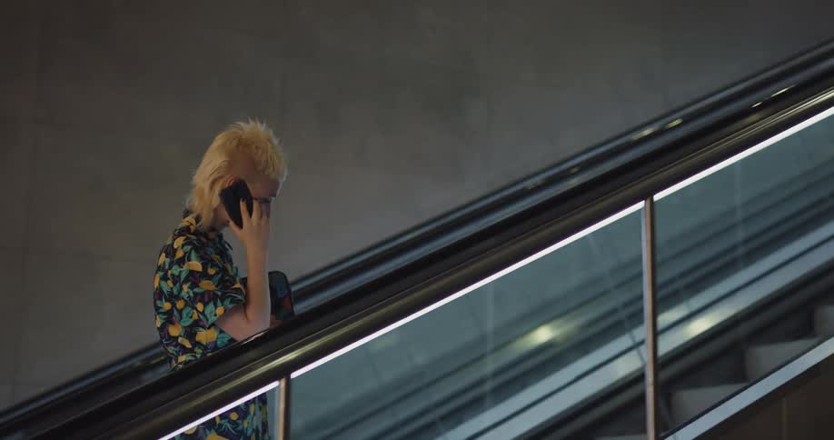 Young blonde female talking on cell phone as she walks on the escalator