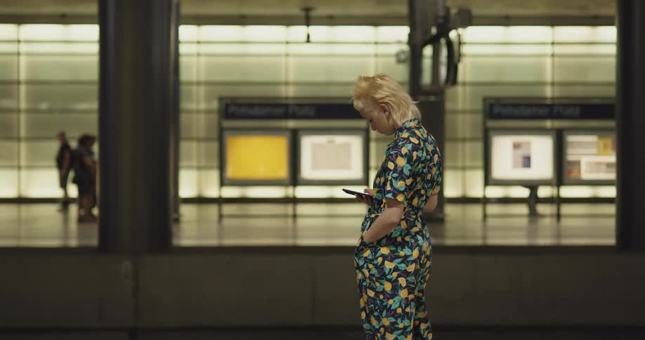 A teenage girl stands on a platform and takes her cell phone out as she waits