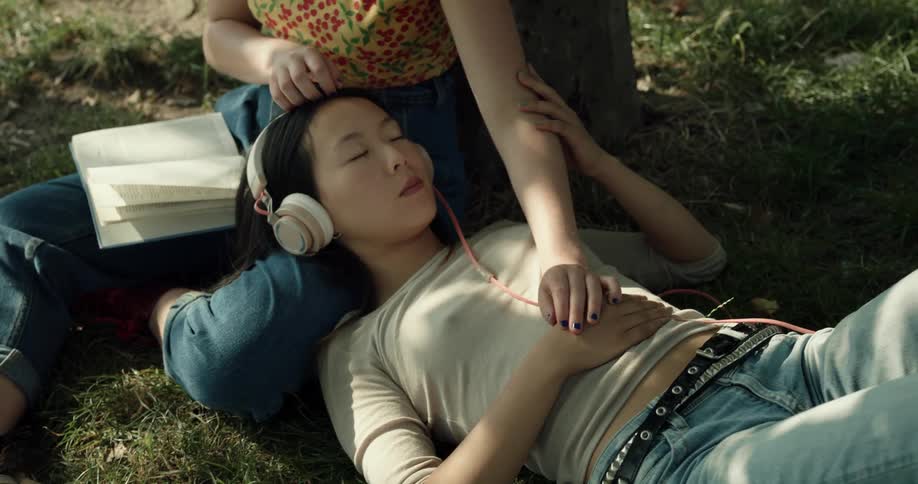 Two women are relaxing in the park as one reads and one listens to music