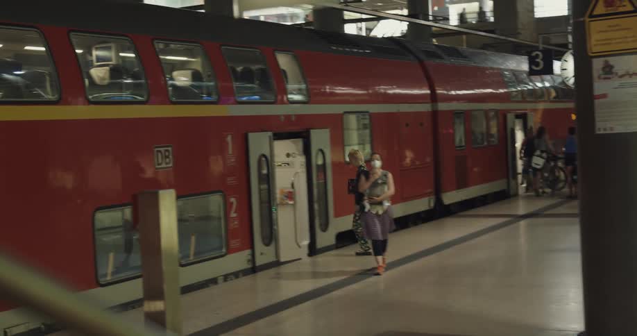 Blonde woman boards train as mother wearing mask disembarks carrying child