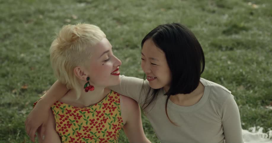 A pair of women smile into the camera while embracing until one woman looks away to kiss the other on the cheek