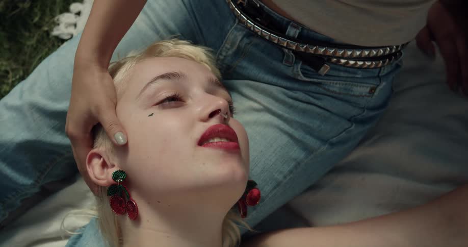 Woman sitting on blanket on grass strokes head of blonde women lying against her lap