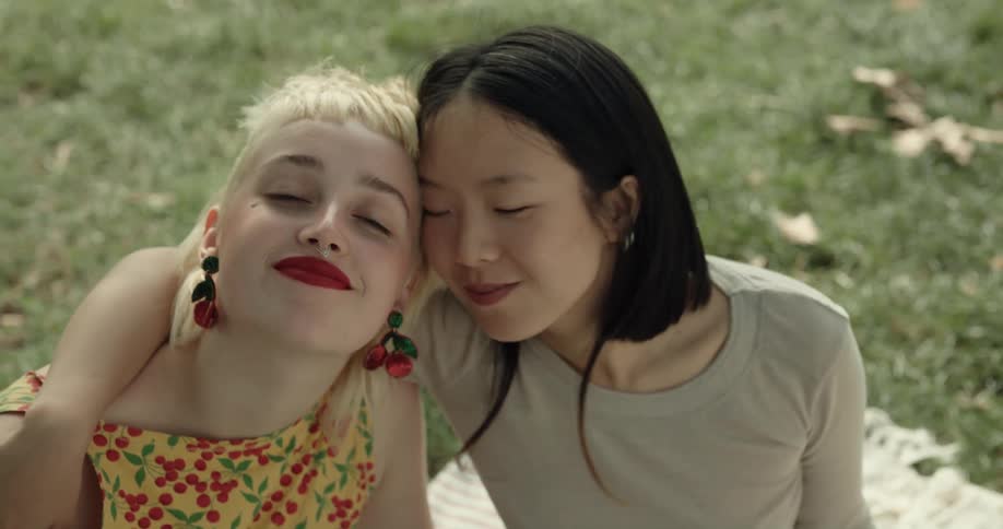 Two women are sitting outdoors in the grass and hugging
