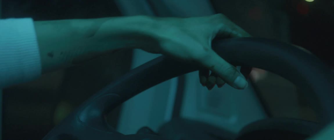 Hand of a man over the steering wheel of a moving vehicle at night