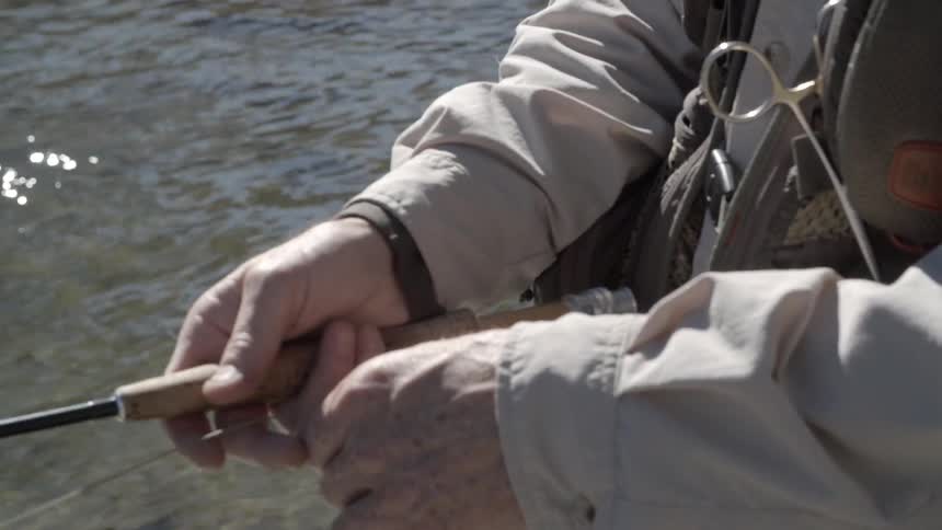 A fisherman pulls on his fishing line while standing in a stream