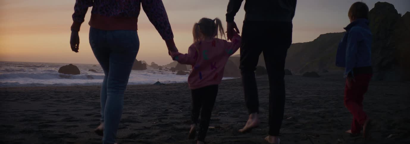 Couple walking on the beach holding hands with kids at sunset