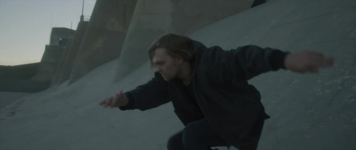 Young long haired blonde man slides down a concrete structure on a channel at sunset