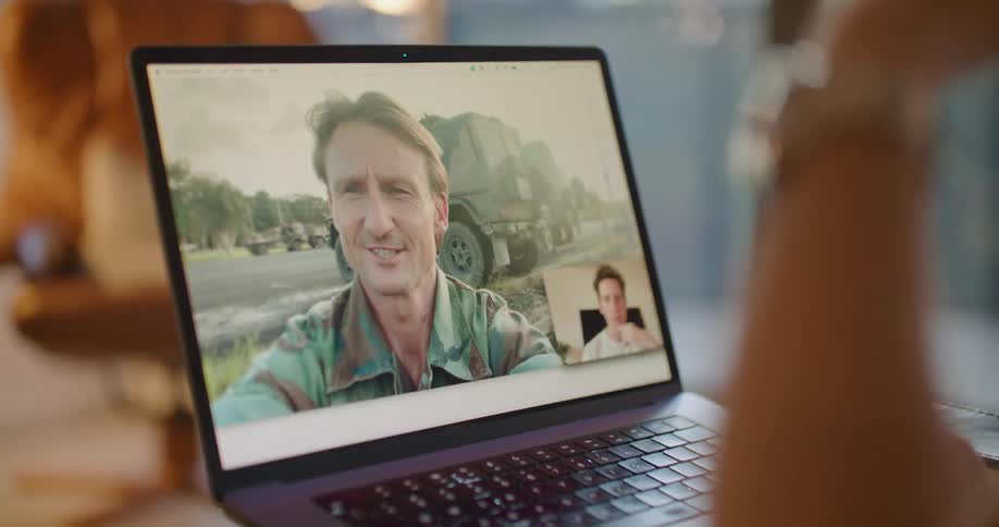 A man is having a video conversation with another man on a laptop computer and the man on the screen blows him a kiss