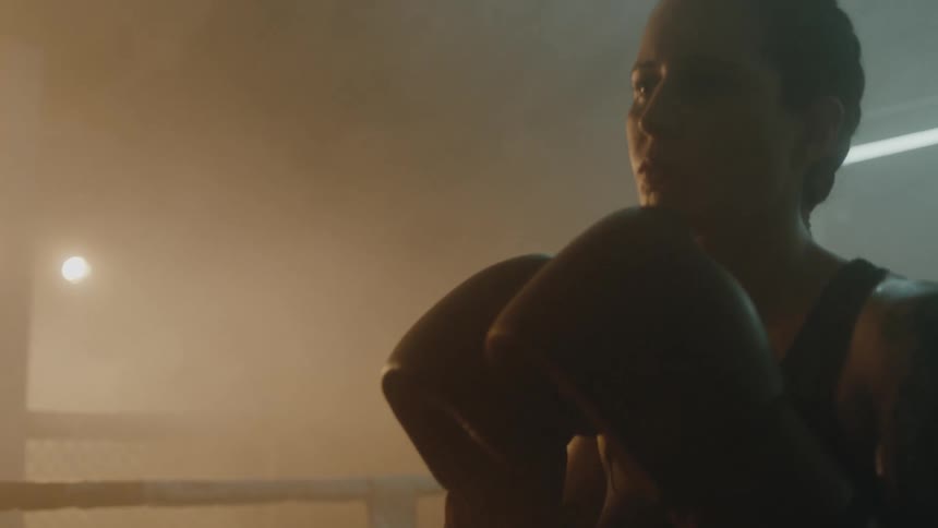 Female boxer with braids sports bra tattoo and boxing gloves keeps her guard up in boxing ring