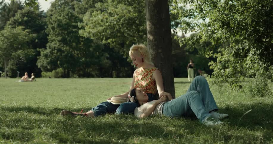 Young couple resting over the green grass under a tree in a park at daytime