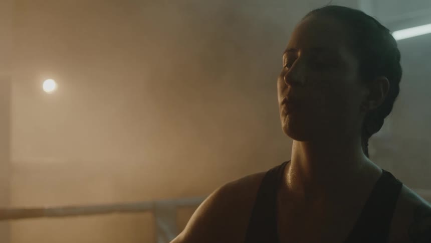 Determined female boxer with braids sports bra and tattoo stands in boxing ring