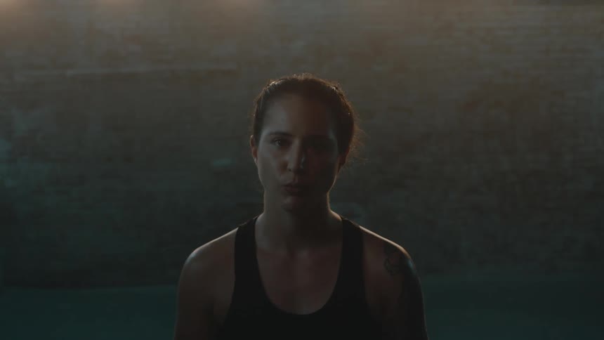 Female boxer with boxing gloves boxing trunks and and braids looks at camera in boxing ring
