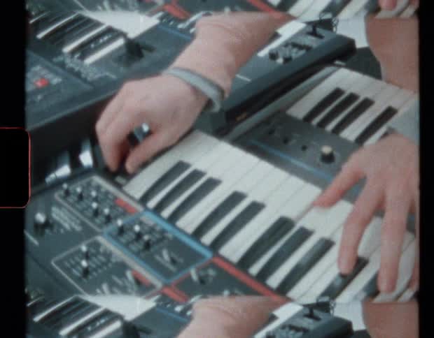 Person wearing a pink sweater playing electronic keyboard at home caught on vintage film