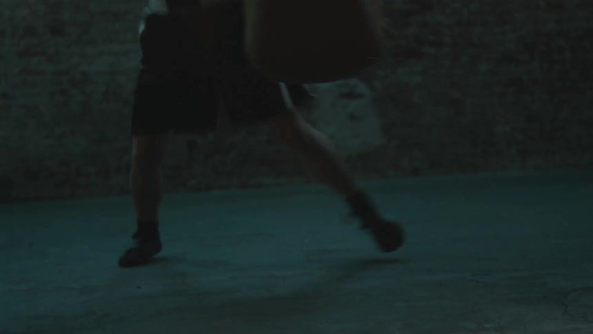 Female boxer with black boxing trunks and shoes hits punching bag in the gym