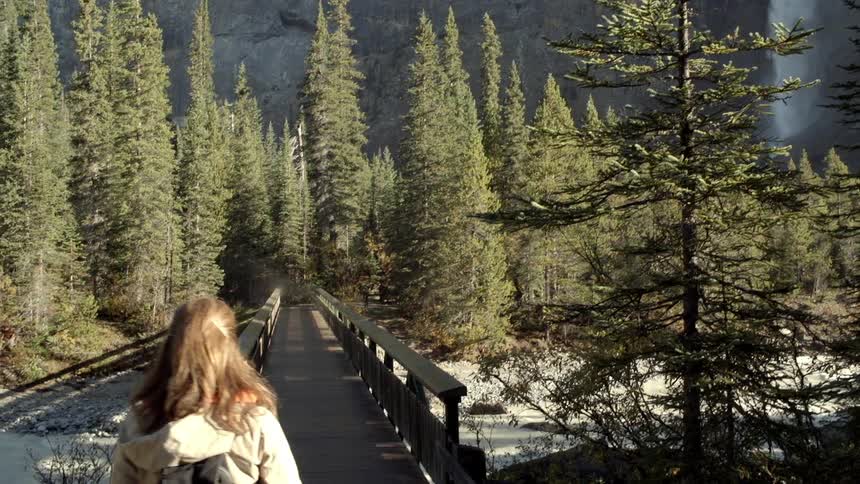 A woman walks towards a mountain with a waterfall
