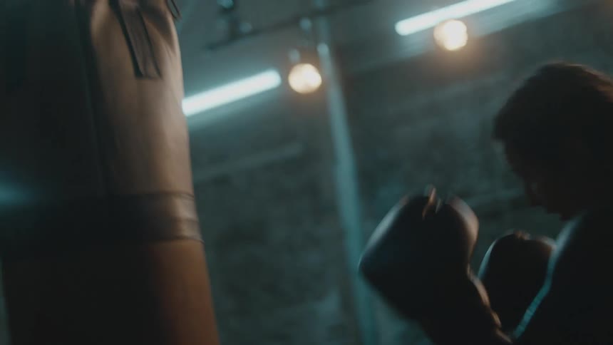 Female boxer with braids sports bra fight trunks and boxing gloves hits puching bag in the gym