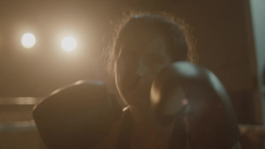 Female boxer with boxing gloves and sports bra trains in the boxing ring