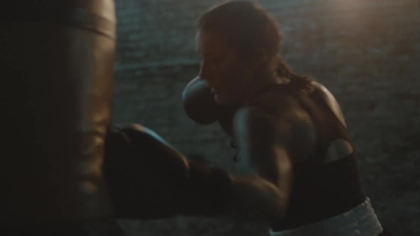 A woman is boxing and hitting a punching bag indoors