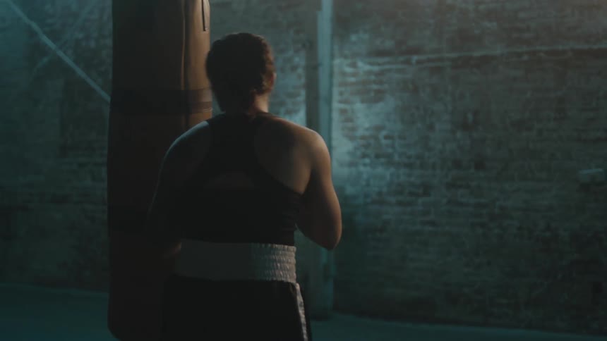Female boxer with braids sports bra fight trunks and boxing gloves hits puching bag in the gym