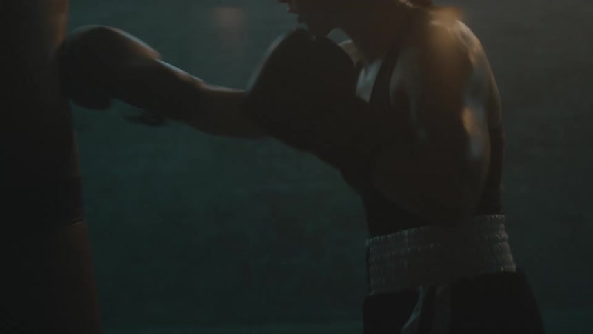 Female boxer with braids sports bra fight trunks and boxing gloves hits puching bag in the gym