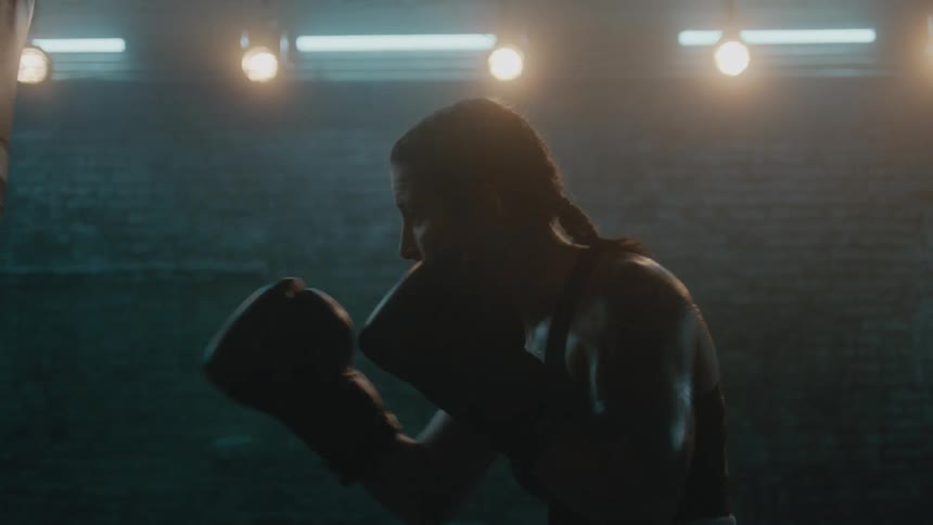 Female boxer wearing a sports bra rapidly hits punching bag in the gym