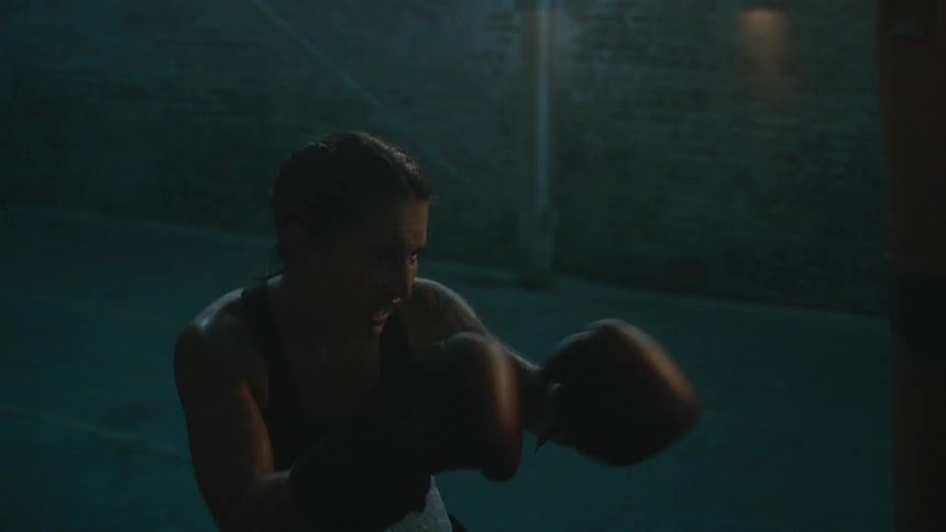 A woman is boxing alone in a dark lit room