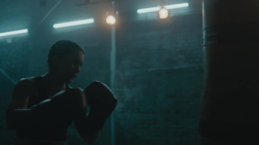 A woman is punching the heavy bag in the gym