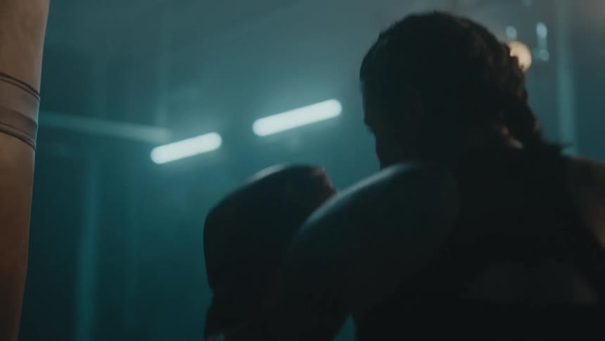 Female boxer with braids sports bra fight trunks and boxing gloves hits puching bag in the gym
