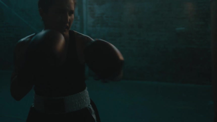 A woman punches a punching bag fiercely with boxing gloves