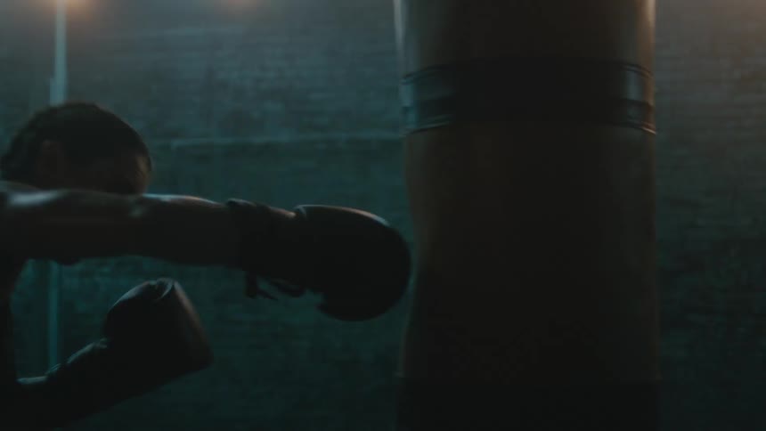 A woman has boxing gloves on as she punches a bag