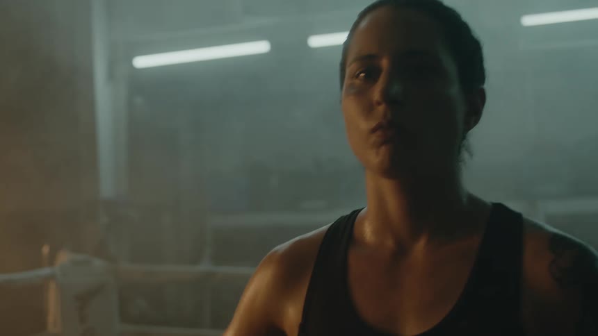 Determined female boxer with braids tattoo and sports bra stands in boxing ring
