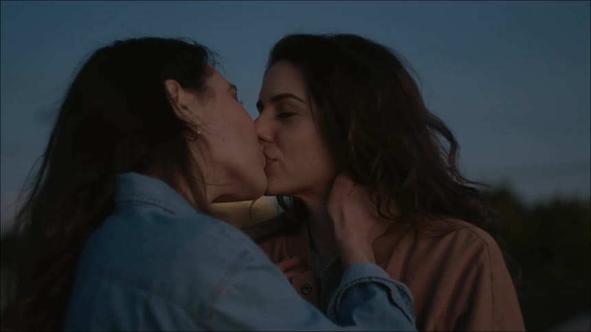 Female couple standing outdoors near woods smile and kiss