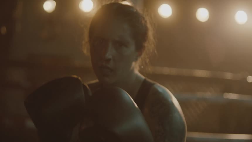 Female boxer with braids boxing gloves and sports bra throws punches at camera in the ring