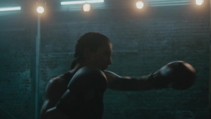 A woman is boxing by herself in a dimly lit room