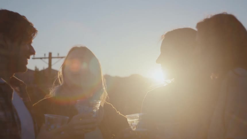 A group of friends are drinking together outdoors while the sun sets on a rooftop