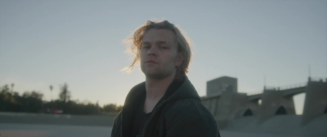 Young long haired blonde man looking at the camera at sunset wearing a hoodie