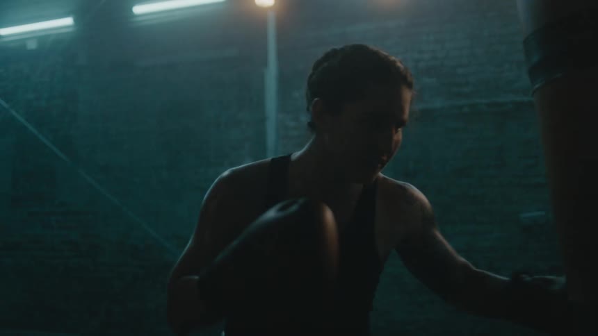 A female boxer trains by striking a punching bag in a dimly lit room
