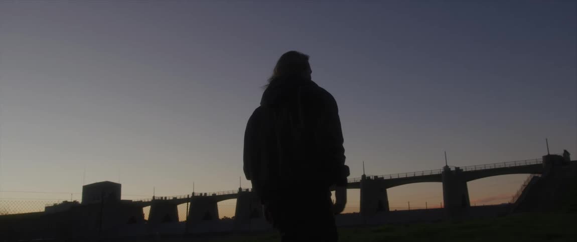 The silhouette of a man walking toward a pier bridge at sunset