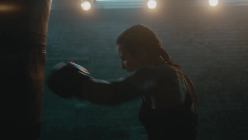 A female boxer rapidly strikes a punching bag in a dimly lit room