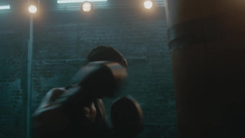 A woman hits a punching bag in a dimly lit gym
