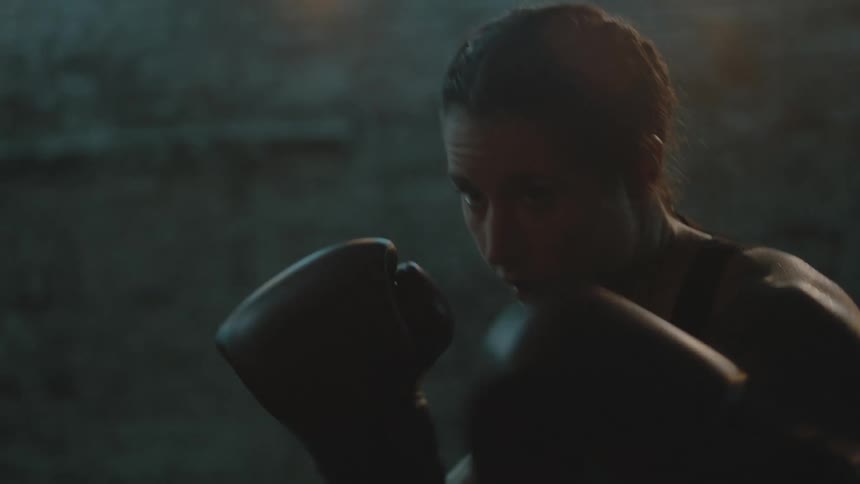 A female boxer trains by striking a punching bag in a dimly lit room