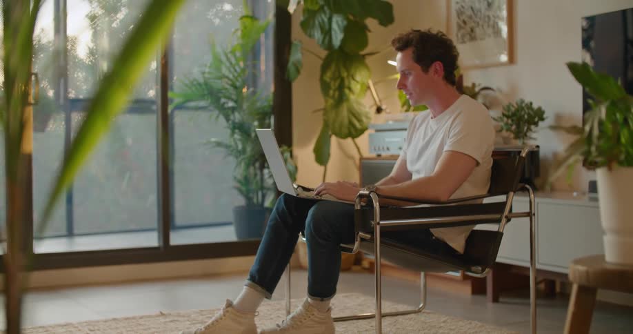 A man is sitting in a chair with a laptop computer having a video conversation with someone
