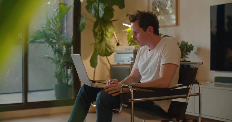 A man is sitting in a chair with a laptop computer having a video conversation with someone