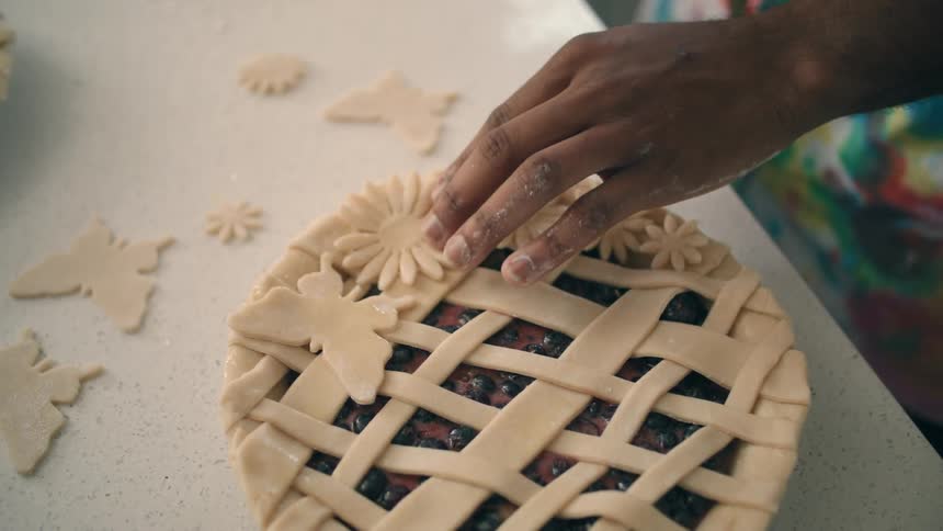 A man applies an eggwash to the back of a pastry dough flower before applying it to a pie ready for baking