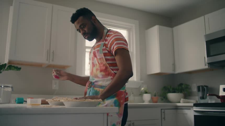A man uses butter to add things to the top of a pie he is creating
