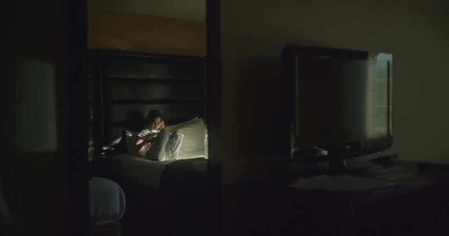 Girl with jeans and shirt sits on bed using smarthone in the bedroom