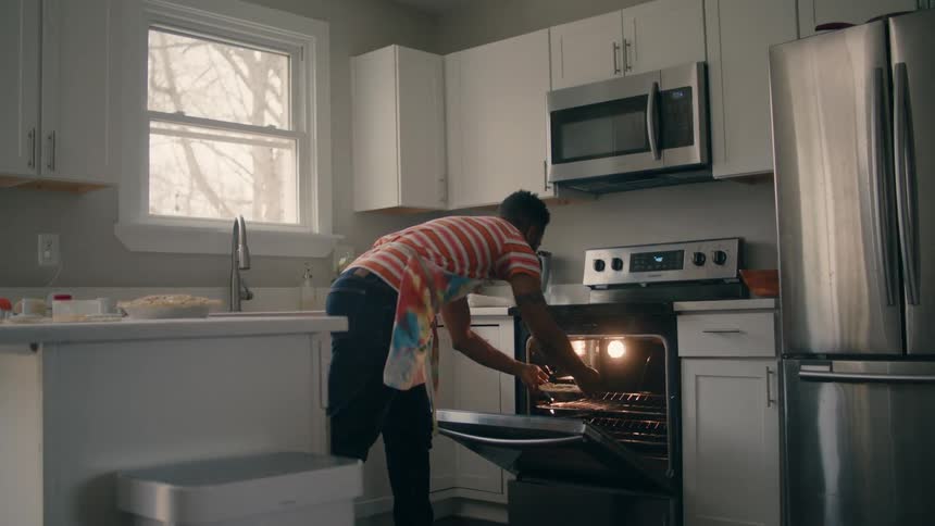 A man places a pie into an oven in a home kitchen during the day
