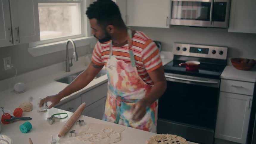 Man wearing an apron cutting pastry circles while baking a pie
